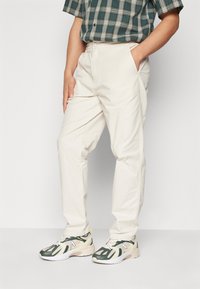 Pantalons légers beiges avec une taille élastique et des poches latérales, associés à des baskets vertes et jaunes avec des accents en maille.