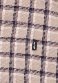 Geruite stof in zachte beige, roze en bruine tinten. Kenmerkt zich door een subtiele textuur met donkere marineblauwe accenten. Bevat een label met de tekst "J&JOY."