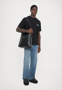 Schwarze Leder-Tasche mit einem hohen, strukturierten Design. Verstellbarer Schulterriemen, flacher Boden und glatte Oberfläche. Lässige Kleidung und Jeans.