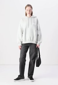 Lys grå hettegenser med frontlomme og logo. Kombinert med mørk grå denim og svarte joggesko. Svart skulderveske med stroppeaksenter.