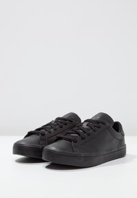 Black leather sneakers with a smooth texture, round toe, flat black rubber sole, and lace-up front. Simple design, no visible patterns or accents.