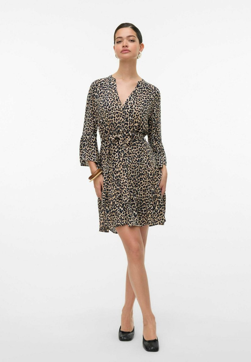 Robe en imprimé léopard dans des tons de beige et de noir, avec un design enveloppant, des manches évasées et une taille cintrée, se terminant au-dessus du genou.