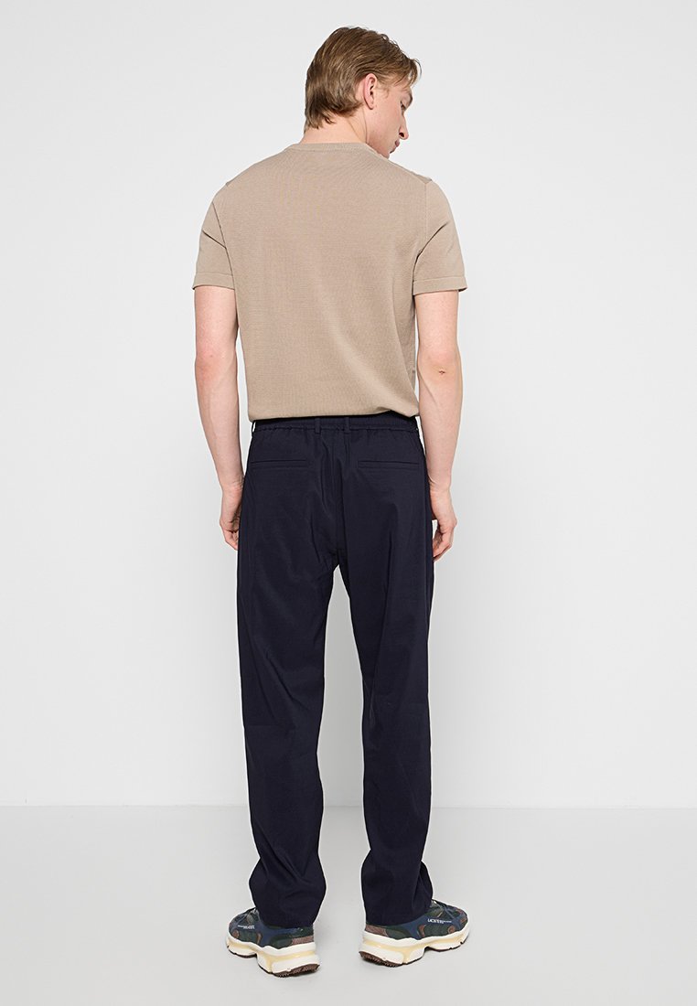Beżowa koszula z krótkim rękawem w połączeniu z granatowymi spodniami. Spodnie mają elastyczny pas i luźny krój, wykonane z lekkiego materiału.