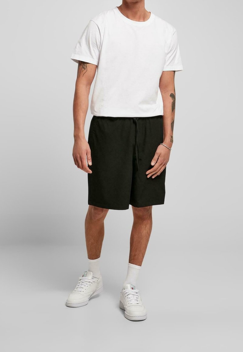 T-shirt blanc à manches courtes et short élastique noir. Le t-shirt est de couleur unie ; le short a un cordon de serrage et une coupe décontractée. Des baskets blanches complètent le look.