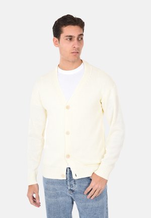 Cardigan color crema realizzato in tessuto a maglia, con scollo a V, cinque bottoni e polsini a coste. Abbinato a denim blu chiaro.