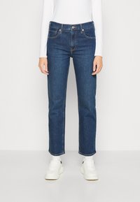 Modré džíny z denimu s rovným střihem a jemným šisováním. Mají přední kapsy, zipový zip a střední pas. Kombinované s bílými teniskami.