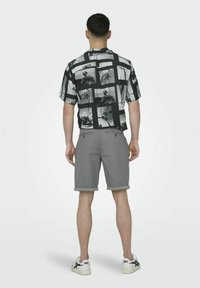 Cămașă cu mânecă scurtă, cu un model alb-negru și un design în carouri, asortată cu pantaloni scurți gri pliați și adidași albi.