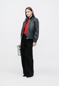 Black leather bomber jacket with ribbed cuffs, paired with a red top and high-waisted black jeans. Holding a black and white snake-patterned bag.