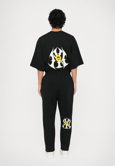 Ensemble t-shirt noir oversize et pantalon de survêtement, avec des motifs graphiques en flamme blanche et jaune au dos et sur la jambe. Matière en mélange de coton.