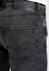 Jeans de Denim negro con un bolsillo trasero con costuras sutiles, una etiqueta de cuero negro texturizado que dice "GABBIANO" y un diseño de corte ajustado.