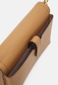 Sac à main en cuir tan avec fermeture à rabat, texture lisse et un seul compartiment intérieur avec une doublure discrète. Accents en matériel doré.