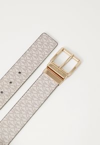 Gepatternter Gürtel in hellem Beige mit strukturiertem Finish, ausgestattet mit einer goldenen Metallschnalle und rechteckigem Krampen. Fünf verstellbare Löcher.