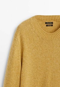 Musztardowo-żółty sweter z dzianiny z prążkowanym, okrągłym dekoltem, o fakturowanym wykończeniu i luźnym kroju. Wewnątrz widoczna metka.