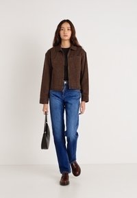 Ruda raštuota striukė dėvima ant juodo viršutinio drabužio, derinama su mėlynomis džinsinėmis ir rudais batais. Modelis laiko juodą rankinę; vienspalvis šviesus fonas.