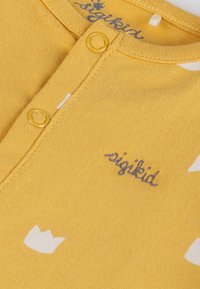 Camicia gialla di cotone con motivi a corona bianca, con scollo henley e due bottoni gialli. Logo "sigikid" in cucitura grigia.