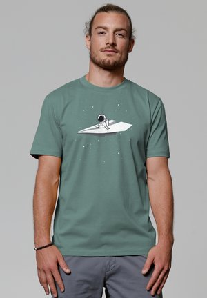 Groen katoenen t-shirt met een graphic van een astronaut op een papieren vliegtuigje, met sterren op de achtergrond en korte mouwen.