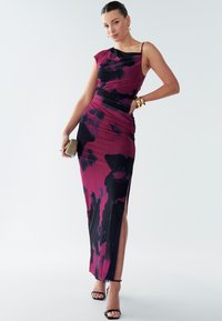 Maxi-jurk in een bloemenverloop van donkerpaars en fuchsia, met een aansluitende bodice, asymmetrische halslijn en een zijsplit. Platte sandalen met bandjes.