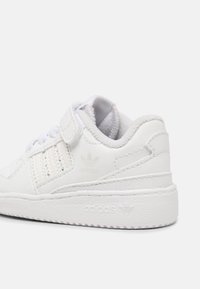 White leather sneaker with textured accents, adjustable strap, and embroidered logo. Features a rubber sole and padded collar for comfort.