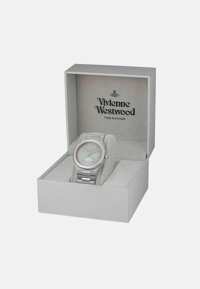 Zilveren metalen horloge in een grijze doos heeft een pastelgradiënt wijzerplaat, numerieke markeringen en een gepolijste metalen band die rust op een zachte kussen.