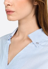 Gestreiftes blaues Hemd mit Kragen, das dekorative Knopfakzente und eine weiche Stofftextur aufweist.