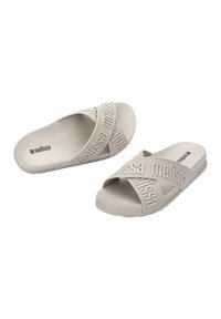 Sandales à enfiler beige avec deux brides croisées portant le nom de la marque en lettres en relief. Fabriquées en caoutchouc souple avec une semelle plate.