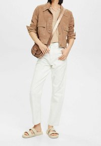 Veste en suède marron, haut beige, jeans blancs taille haute, et sandales beiges. Sac bandoulière avec une finition texturée. Tenue simple et décontractée.