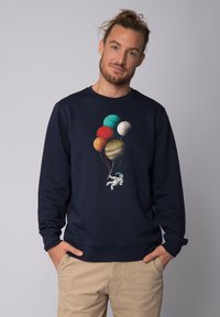 Sweat-shirt bleu marine présentant un astronaute tenant des ballons en forme de planètes colorées, conçu avec des textures et motifs vifs.
