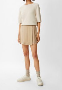 Beige ribbet sweater med brede ærmer kombineret med en beige miniskørt. Hvide sneakers og lyse, strukturerede sokker fuldender outfittet.