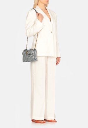 Blazer bianco su misura, pantaloni ampi abbinati, sandali arancioni e una borsa grigia con texture e tracolla in catena metallica.