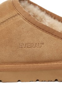 Tan suede slipper featuring a soft interior lining, a textured exterior, and molded rubber sole with a logo embossed on the side.