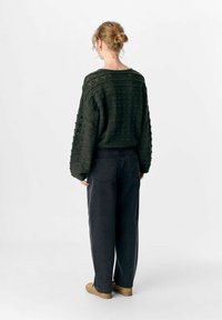 Donkergroen gebreide trui met een textuurpatroon, verlaagde schouders en een losse pasvorm, gecombineerd met hoge zwarte jeans.