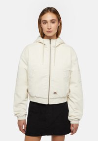 Cremefarvet cropped jakke med hætte, lynlås, ribbede ærmer og logo-patch. Lavet af struktureret stof og har et afslappet design.