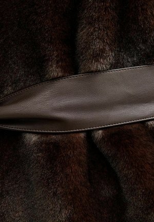 Pelliccia marrone con una consistenza morbida, unita da una fascia di cuoio marrone liscia, creando un design a strati. Gli accenti in cuoio sono rettangolari e piatti.