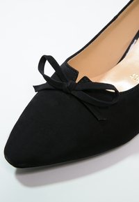 Chaussure plate en daim noir à bout pointu avec un petit nœud décoratif à l'avant et une doublure intérieure beige.