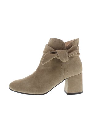 Suede ankle boot in light brown with a wide block heel, curved silhouette, and a bow detail at the ankle. Smooth texture and stitched accents.