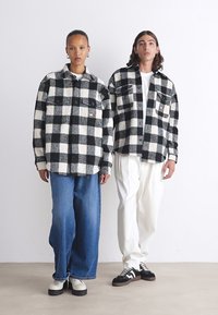 Ternet sort og hvid flannel skjorter med to brystlommer, parret med blå jeans og hvide bukser, iført sorte og hvide sneakers.