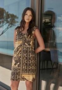 Vestido corto con un diseño de patrón negro y dorado que presenta elementos florales y geométricos, y detalles de volantes en los hombros.