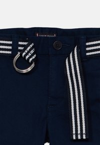 Pantalon bleu marine avec une ceinture en tissu rayé noir et blanc passant dans les passants, sécurisée par une boucle métallique double en D.
