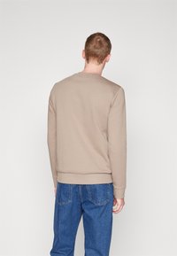 Beige sweatshirt med rund halsringning, ribbade muddar och fåll. Bärs tillsammans med blå denimjeans som har en slät textur och en avslappnad passform.
