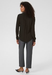 Camicia nera a maniche lunghe con orlo arrotondato, abbinata a pantaloni grigi a gamba dritta e scarpe nere con cinturini e tacco. Tessuto liscio.