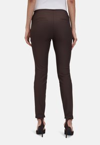 Brązowe spodnie slim fit wykonane z elastycznej tkaniny, z kieszeniami i gładką fakturą, w połączeniu z czarnymi szpilkami.