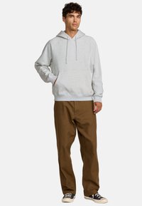 Szary kaptur z kieszenią kangurką, w połączeniu z brązowymi spodniami i czarnymi sneakersami. Posiada sznurki i ribbed cuffs.