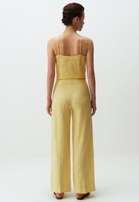 Geel linnen crop top met verstelbare bandjes, gecombineerd met wijduitlopende gele linnen broek, met een ontspannen pasvorm en minimale naden.