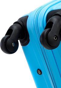 Valise rigide bleue avec une surface texturée, roues noires et fermeture éclair. Détails notables incluent une couture lisse et des accents en métal.