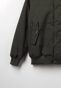 Olivengrøn bomberjakke, struktureret stof, elastiske manchetter og kant, sidelomme med klap og trykknaplukning.