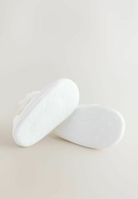 Valged pehmed sussid, millel on tekstureeritud välistald südame mustritega ja lillede aksent ülaservas.