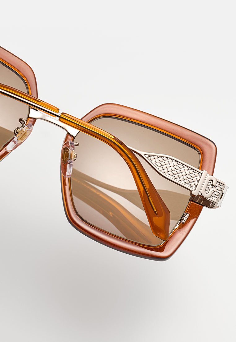 Lunettes de soleil carrées avec des lentilles dégradées brunes, une monture en plastique ambre et des accents en métal argenté, présentant un motif texturé sur les branches.