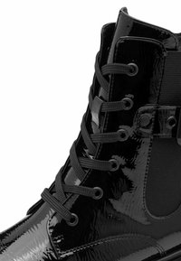 Glänzender schwarzer Lederkampstiefel mit runder Zehenform, schwarzen Schnürsenkeln durch Metall-Ösen und elastischen Seitendetails.