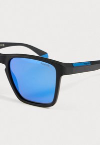 Mustat suorakulmaiset aurinkolasit, joissa on siniset peilipinnat ja Polaroid-brändäys linsseissä ja sankoissa.