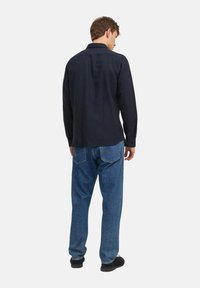 Mørkeblå skjorte med knap, krave, lange ærmer og lige kant, parret med lyseblå løstsiddende jeans og sorte sko.